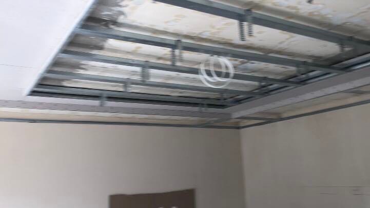 Stelaż metalowy podwieszanego sufitu z widocznymi kablami elektrycznymi, przygotowany do montażu płyt, surowy stan wykończenia wnętrza.