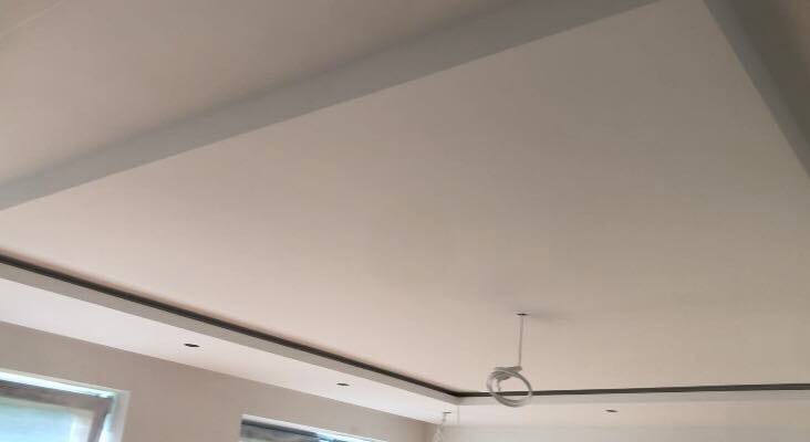 Biały sufit z szarymi listwami wykończeniowymi, widoczne okna w dolnej części kadru oraz wiszący przewód elektryczny.