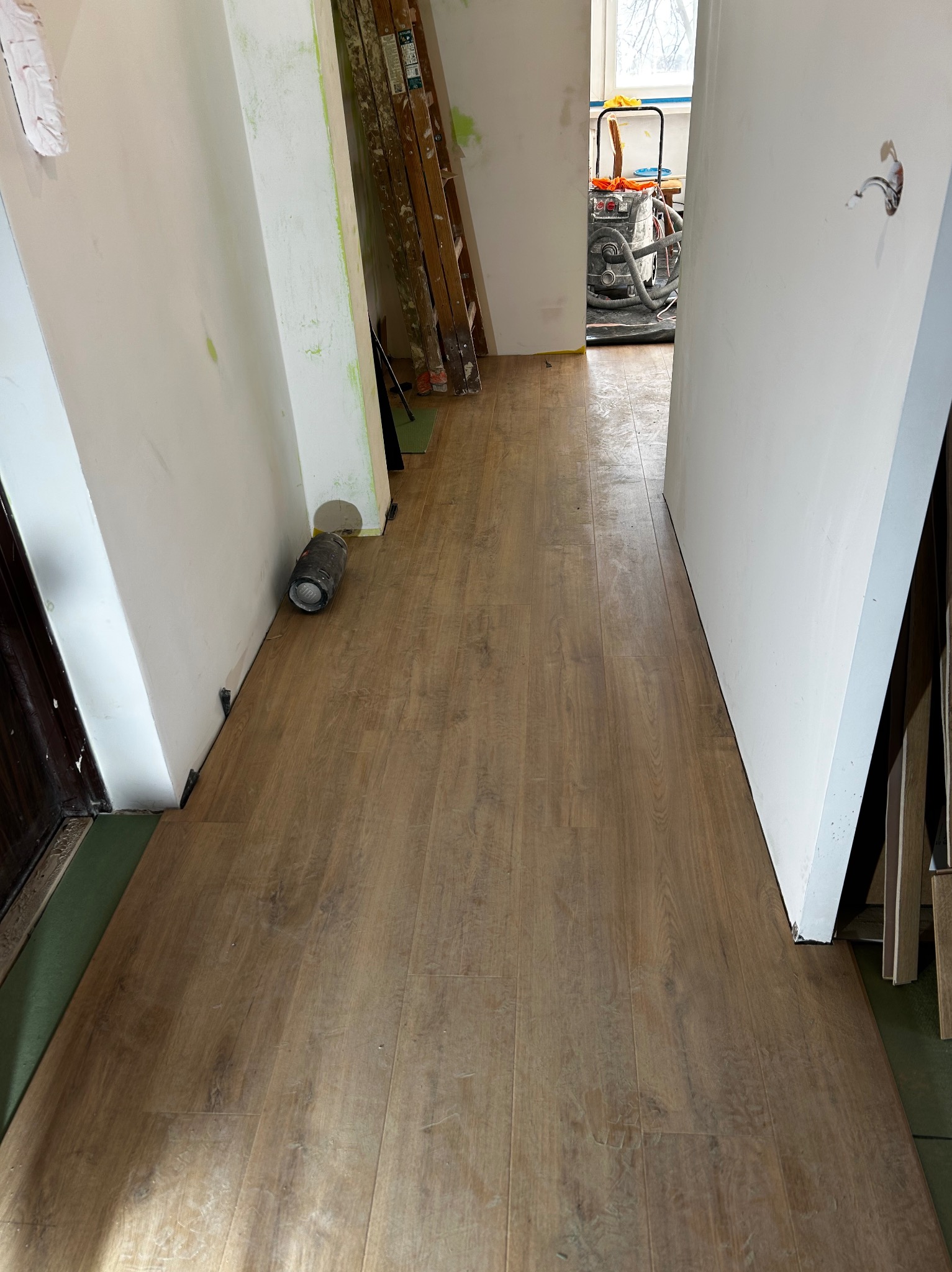 Układanie paneli podłogowych w korytarzu, widoczna podkładka i szczelina dylatacyjna. W tle drabina i maszyna do czyszczenia posadzek.