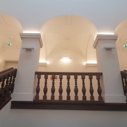 LUNAN SP. Z O.O. - Klatka schodowa z drewnianą balustradą i białymi ścianami, widziana z dołu, z widocznymi sklepieniami łukowymi i oświetleniem LED.