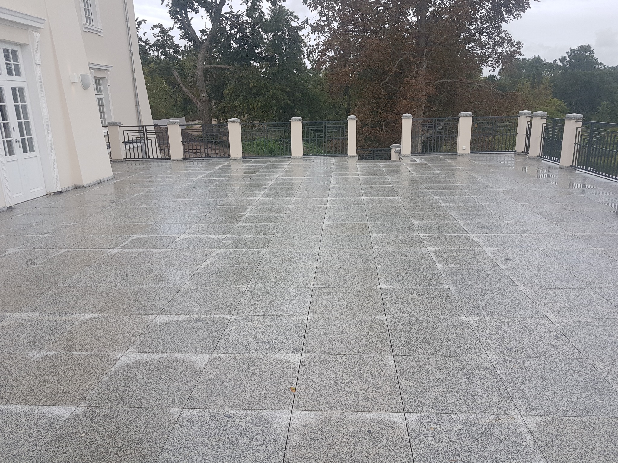 Szary, granitowy taras po deszczu w Warszawie, z widokiem na park i klasyczną architekturę budynku.