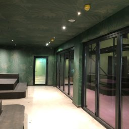 pARt - Wnętrze biura z zielonymi ścianami w tropikalne wzory, czarnymi ramami okiennymi i schodkowymi siedziskami. Sufit z równomiernie rozmieszczonymi punktowymi lampami.