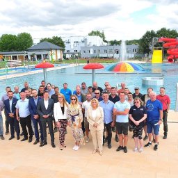 USŁUGI DROGOWE I BRUKARSKIE RADOSŁAW WOJTOWICZ - Grupa ludzi pozuje na tle nowego basenu w Świdnicy, z atrakcjami wodnymi, zjeżdżalnią i fontanną w tle.