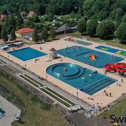 USŁUGI DROGOWE I BRUKARSKIE RADOSŁAW WOJTOWICZ - Kompleks basenów zewnętrznych w Świdnicy, widok z lotu ptaka, obejmujący basen sportowy, rekreacyjny z atrakcjami wodnymi, brodzik dla dzieci oraz czerwoną zjeżdżalnię, otoczony zielenią i budynkami.