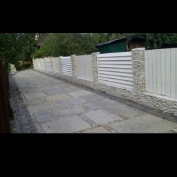 USŁUGI DROGOWE I BRUKARSKIE RADOSŁAW WOJTOWICZ - Nowoczesne ogrodzenie panelowe z elementami kamiennymi w Domaradzu, widoczne z perspektywy chodnika z kostki brukowej.