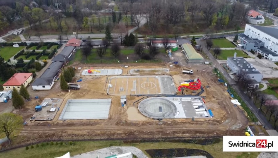 Widok z lotu ptaka na budowę kompleksu basenowego w Świdnicy, z widocznymi nieckami basenowymi w różnym stadium zaawansowania, w tym basen okrągły i zjeżdżalnia wodna; teren otoczony ziemią...