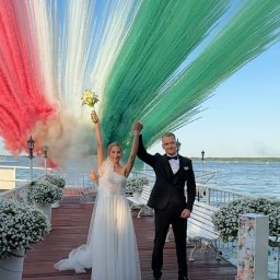 Piotr Wołowik Fotografia - Para młoda na molo, świętująca z kolorowymi pióropuszami dymu w barwach flagi Włoch. Ona w białej sukni, on w smokingu. W tle woda i dekoracje kwiatowe.