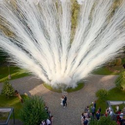 Piotr Wołowik Fotografia - Para młoda w otoczeniu gości i efektownej fontanny iskier podczas ceremonii ślubnej, uchwycone z lotu ptaka. Widoczne drzewa, zaparkowane samochody i dekoracje.