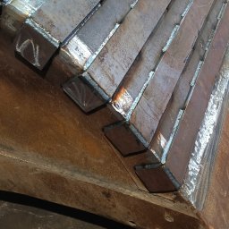 Szymon Hausler - Fragment konstrukcji stalowej z przyspawanymi elementami, widoczne spawy i surowy wygląd metalu.