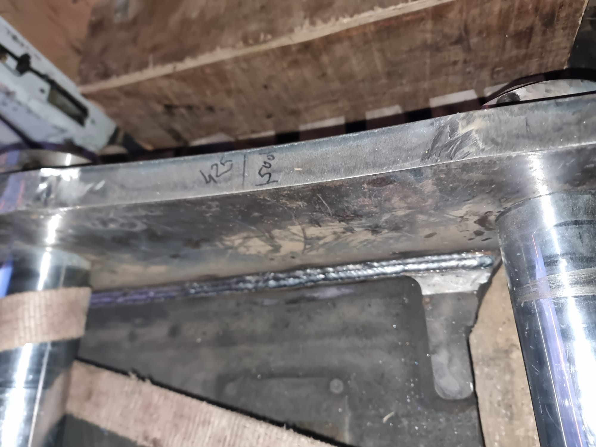 Metalowa konstrukcja w trakcie spawania, widoczne świeże spawy, oznaczenia wymiarów '425' i '500' naniesione markerem na metalu, elementy podtrzymywane pasami transportowymi.