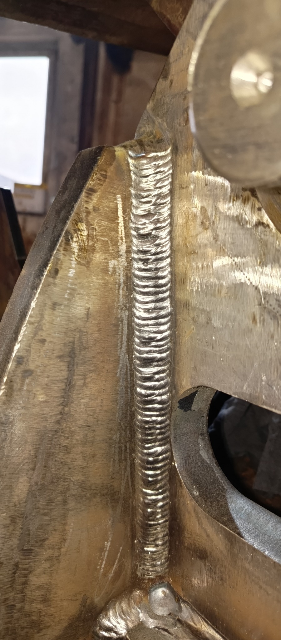 Szczegółowe zbliżenie na spawany element konstrukcyjny z metalu, ukazujące precyzyjne i równe spoiny wzdłuż krawędzi, z widocznymi śladami obróbki metalu i niedoskonałościami powierzchni.