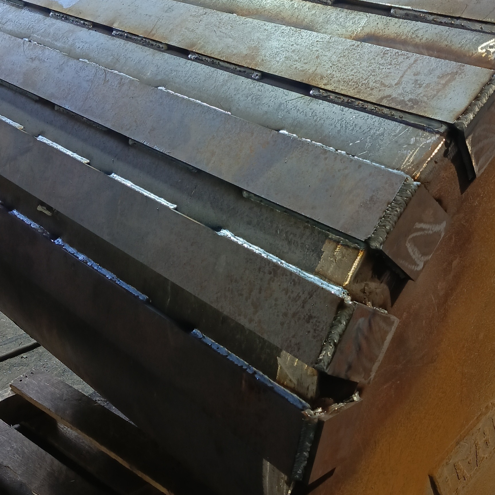 Metalowe profile połączone spawami, ułożone warstwowo, widoczne ślady obróbki i niedoskonałości spoin.