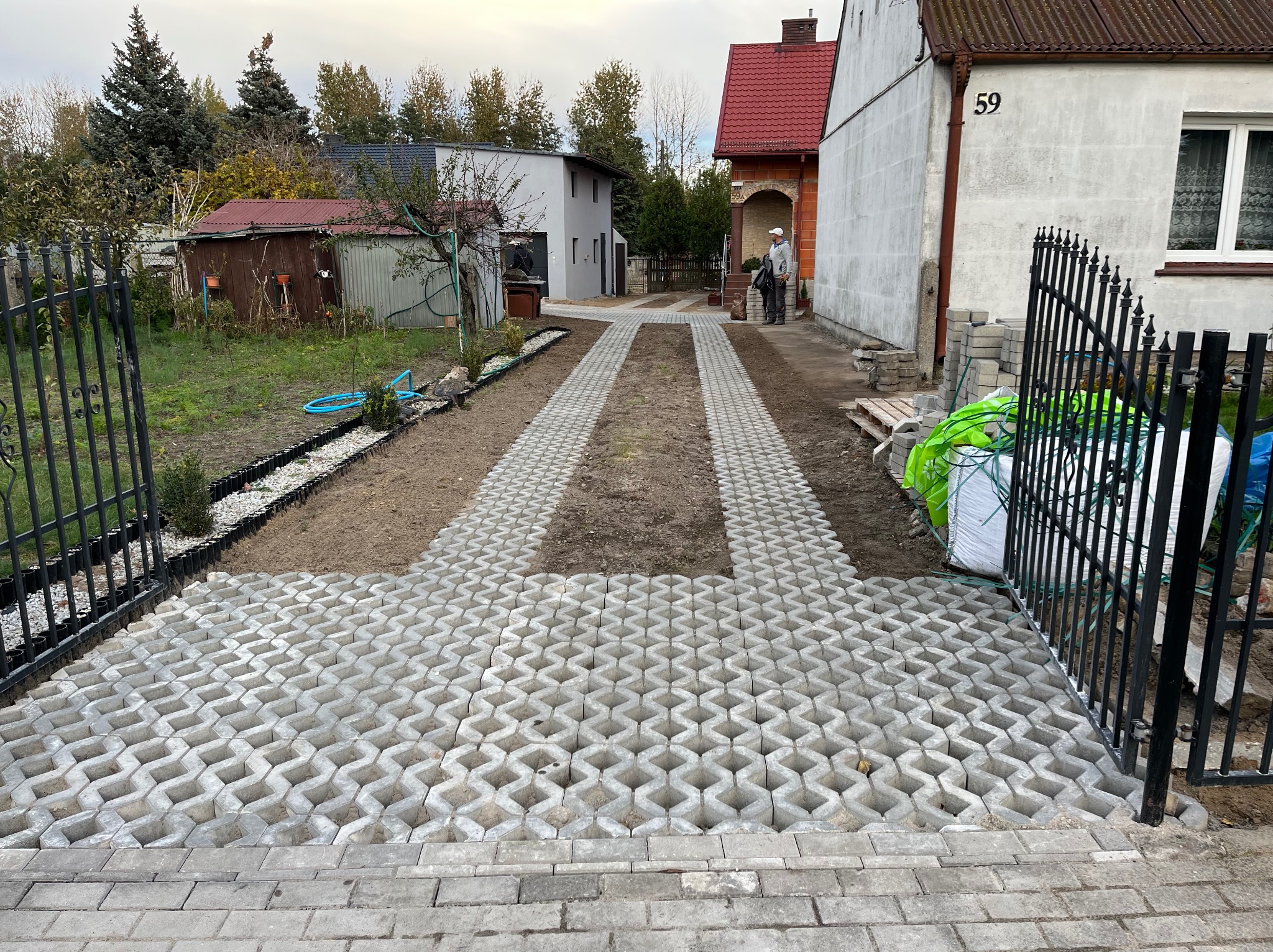 Ułożona ażurowa kostka betonowa na podjeździe do domu z numerem 59, widoczne czarne metalowe ogrodzenie i przygotowany teren pod dalsze prace.