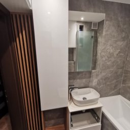 Domostan - Nowoczesna łazienka z marmurowymi płytkami, białą umywalką nablatową, szafką z drewnianymi akcentami i lustrem. Minimalistyczny design z otwartą szufladą.