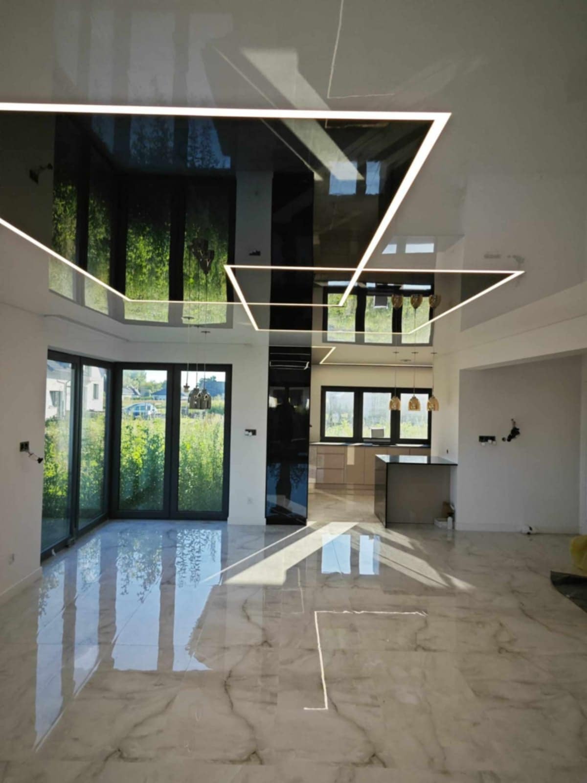Nowoczesne wnętrze: lśniąca podłoga z marmuru, czarny sufit z geometrycznym oświetleniem LED i widok na zieleń za oknem. Minimalistyczny design i przestronność.