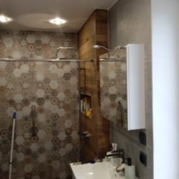 USŁUGI REMONTOWO BUDOWLANE SŁAWOMIR KWASIK - Wykończona łazienka z heksagonalnymi płytkami w odcieniach brązu i szarości, kabina prysznicowa z drewnianą wnęką na kosmetyki, umywalka z białą szafką i lustrem.