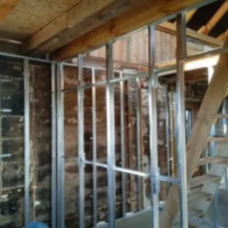 Metalowa konstrukcja szkieletowa pod ścianę działową z płyt kartonowo-gipsowych w surowym wnętrzu z drewnianym stropem i fragmentem schodów.