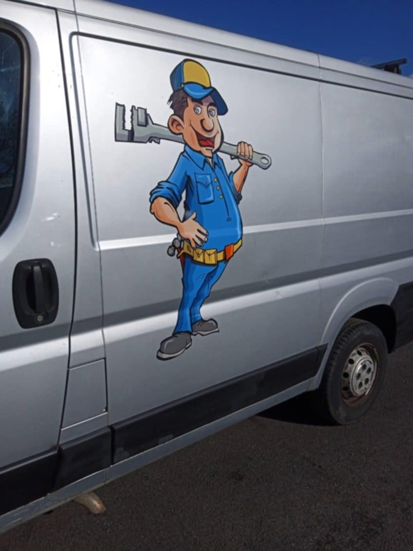 Srebrny van z kreskówkową postacią hydraulika trzymającego klucz francuski, naklejka na karoserii.