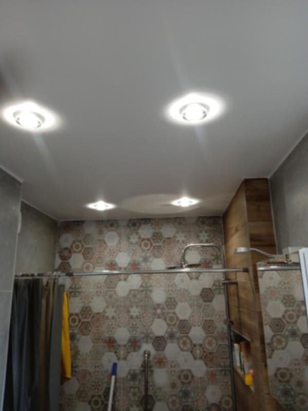 Wykończona łazienka z heksagonalnymi płytkami w odcieniach szarości, brązu i beżu, z zamontowanymi czterema punktowymi lampami sufitowymi i szarą zasłoną prysznicową.