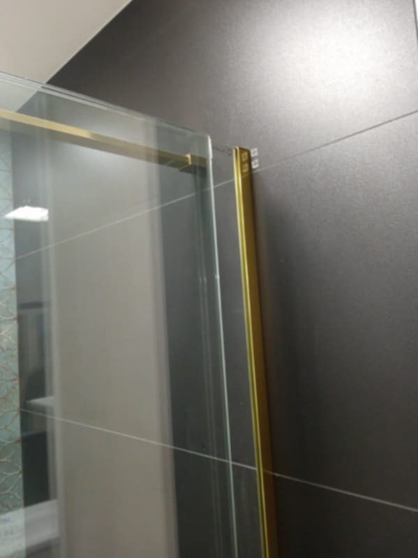 Fragment kabiny prysznicowej z złotymi profilami na tle ciemnych płytek ceramicznych z fugami.