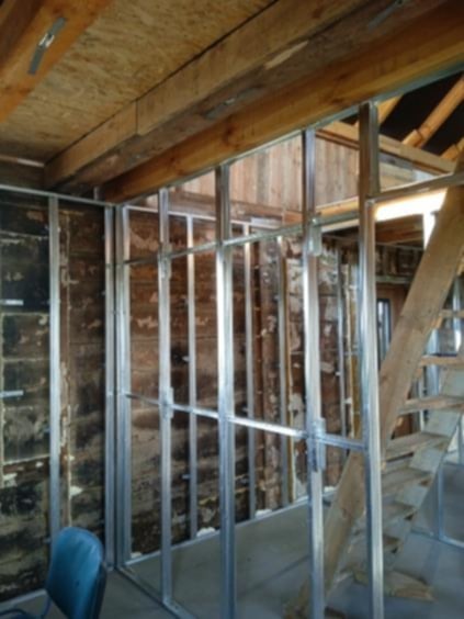 Metalowa konstrukcja szkieletowa pod ścianę działową z płyt kartonowo-gipsowych w surowym wnętrzu z drewnianym stropem i fragmentem schodów.