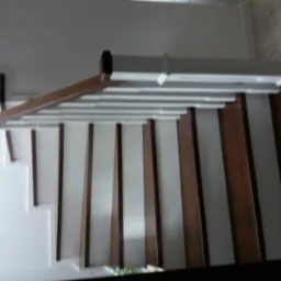 Wewnętrzne schody z drewnianymi stopniami i białymi podstopnicami, brązowa poręcz, widok z dołu, minimalistyczny design.