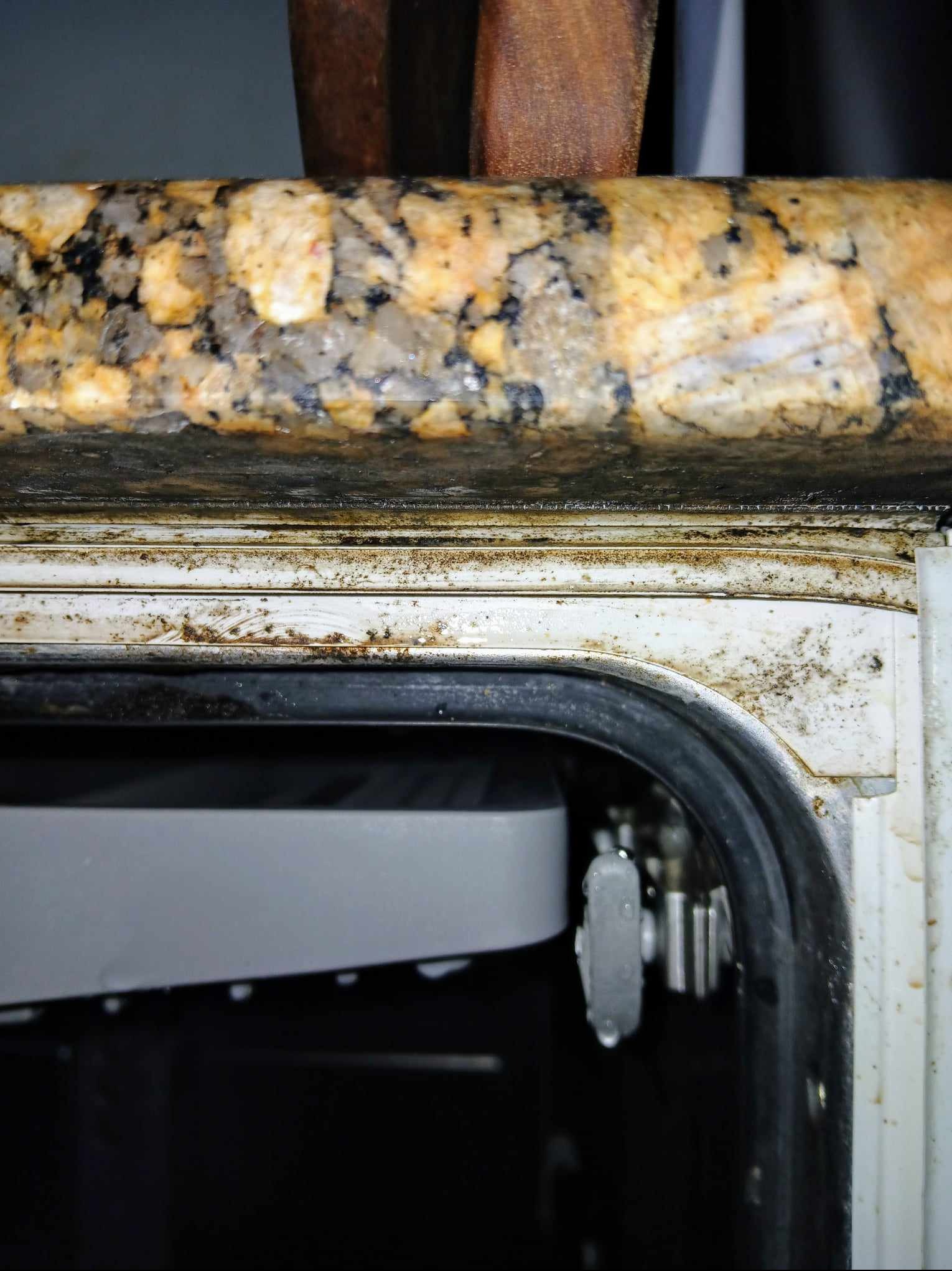 Zabrudzona uszczelka i obudowa zmywarki pod blatem kuchennym z granitu, widoczne plamy i zacieki.