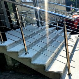 VSM ALUMINIUM PREFABRYKACJA Sp. zoo SPK. - Schody wejściowe z szarego lastryko, zabezpieczone polerowaną konstrukcją z metalu, widoczne odbicia światła na powierzchni.