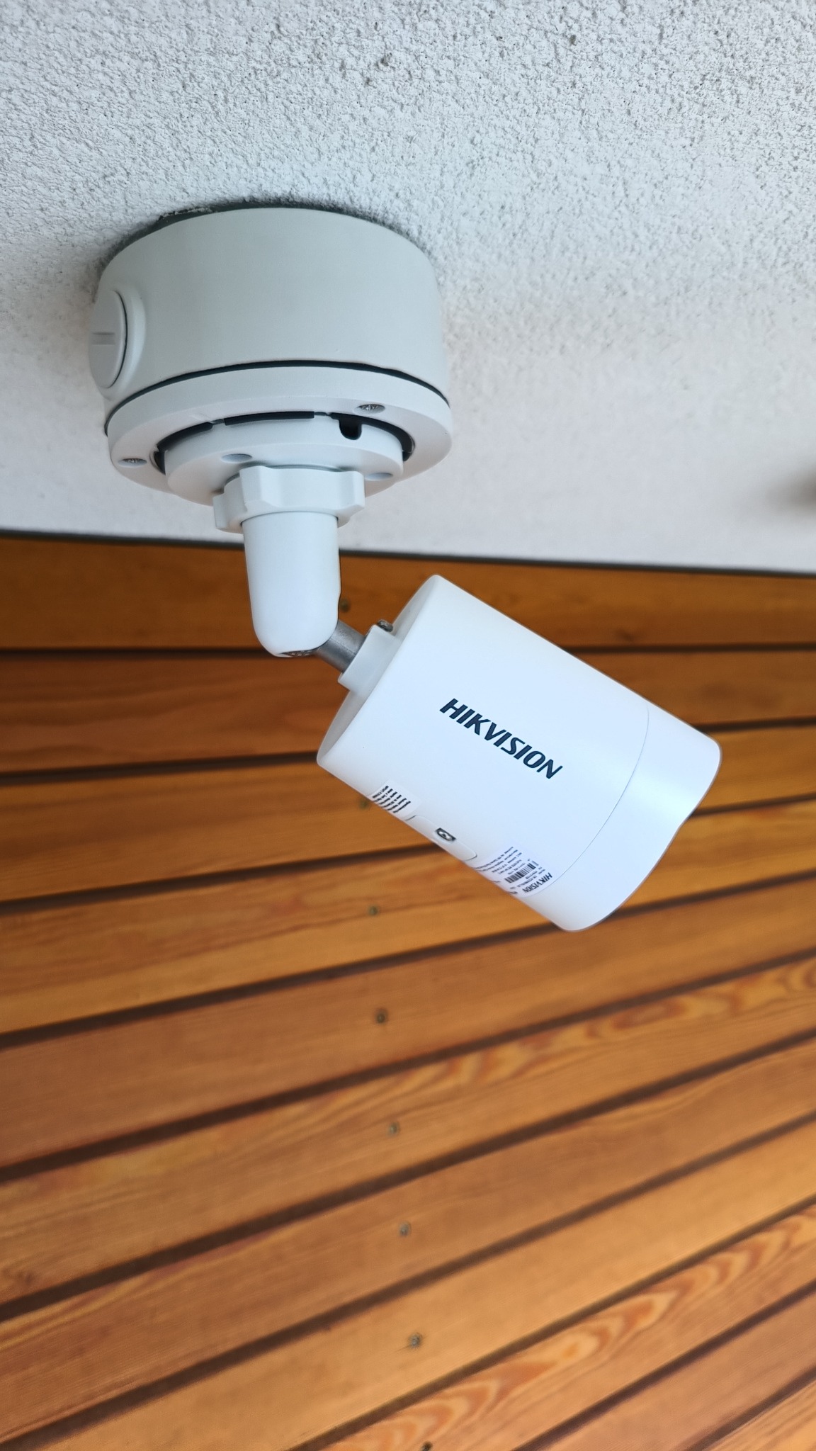 Zamontowana kamera Hikvision na suficie z drewnianą boazerią w tle. Kamera ustawiona pod kątem, widoczne detale mocowania i obudowy.