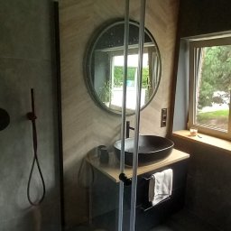 Patryk Sandecki - Nowoczesna łazienka z kabiną prysznicową typu walk-in, okrągłym lustrem, umywalką nablatową i panelami ściennymi w jodełkę.