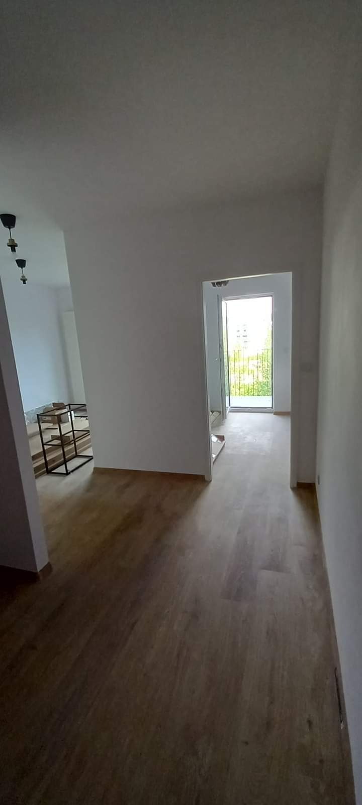 Wnętrze po remoncie: świeżo pomalowane białe ściany, nowa drewniana podłoga, widoczne niedokończone prace w tle i surowe lampy bez kloszy.