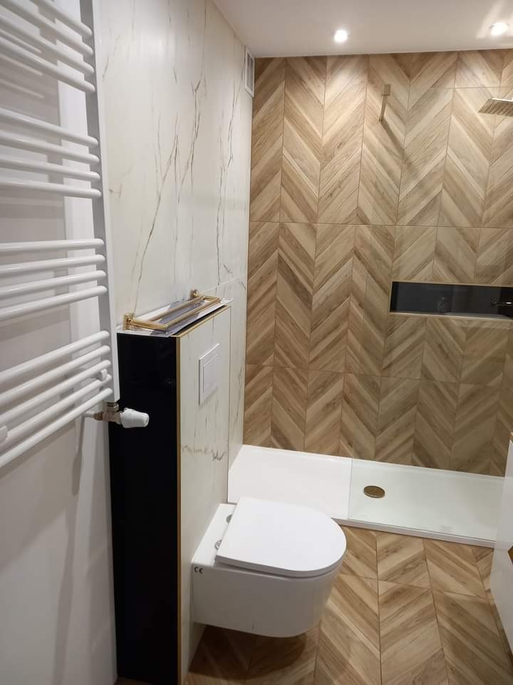 Nowoczesna łazienka z drewnopodobnymi płytkami ułożonymi w jodełkę na ścianie i podłodze, białą armaturą podwieszaną oraz grzejnikiem drabinkowym.