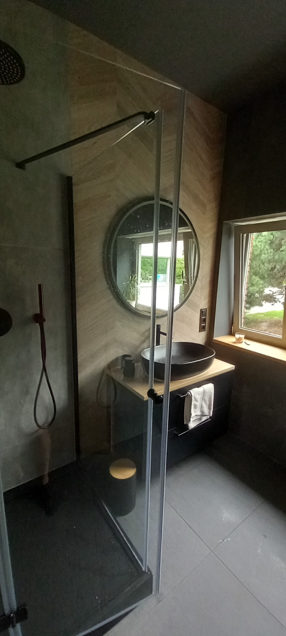 Nowoczesna łazienka z kabiną prysznicową typu walk-in, okrągłym lustrem, umywalką nablatową i panelami ściennymi w jodełkę.