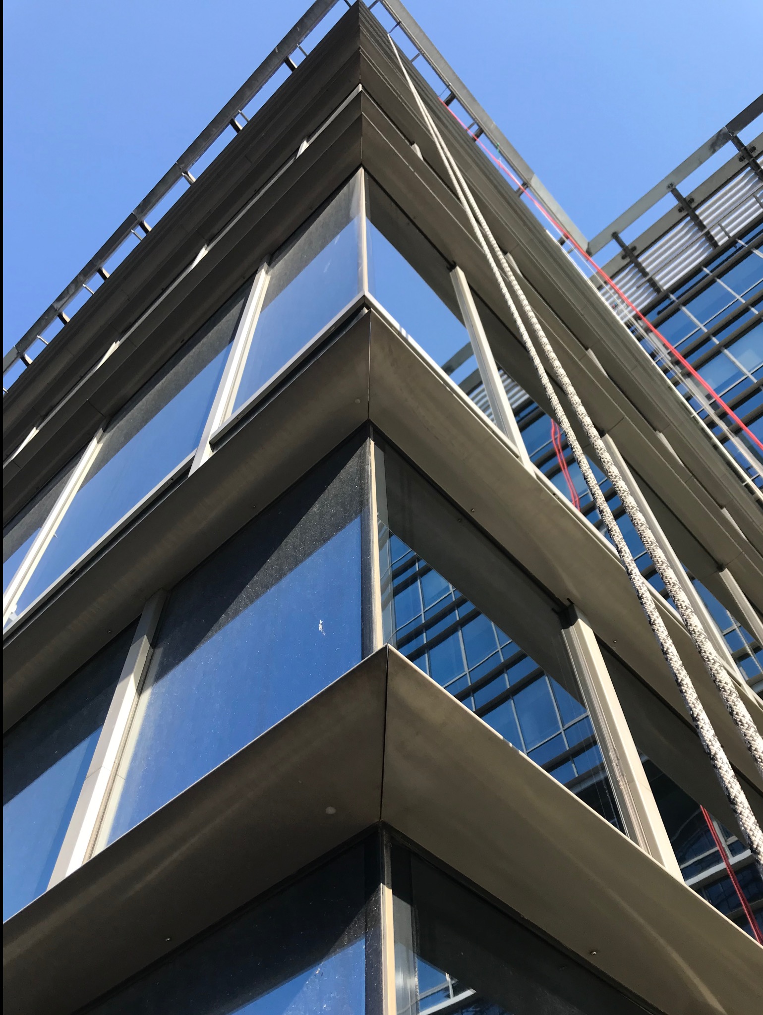 Nisko kątowe ujęcie narożnika przeszklonego biurowca z linami do mycia okien na wysokości, część okien jest brudna.