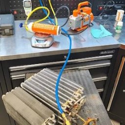 ElexFix Dawid Hłubek - Serwis klimatyzacji: Manometry, pompa próżniowa i filtr na wadze podczas napełniania układu chłodniczego. Widoczna sprężarka i skraplacz.