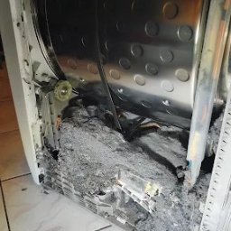 ElexFix Dawid Hłubek - Otwarta pralka z widocznym bębnem i nagromadzeniem szarego brudu/kurzu wewnątrz obudowy. Widoczne elementy konstrukcyjne i fragment podłogi z płytek.