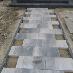 Fragment układania schodów wejściowych z szarej kostki brukowej na podsypce piaskowej. Widoczne obrzeża i częściowo ułożone stopnie.