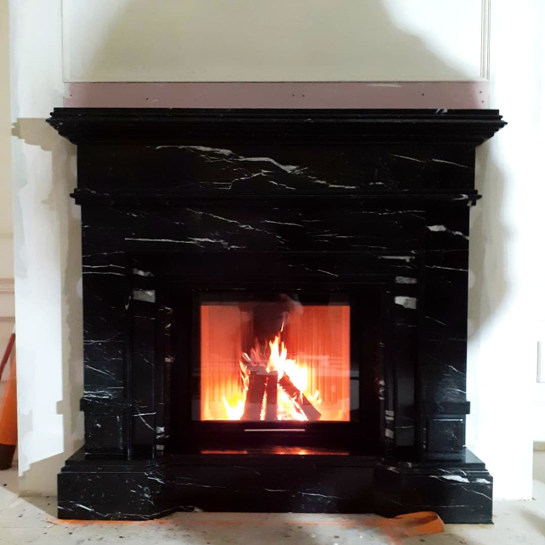 Czarny marmurowy kominek z palącym się drewnem, widoczny w trakcie montażu w Kiełczowie, z pomarańczowymi śladami po zaprawie na podłodze.