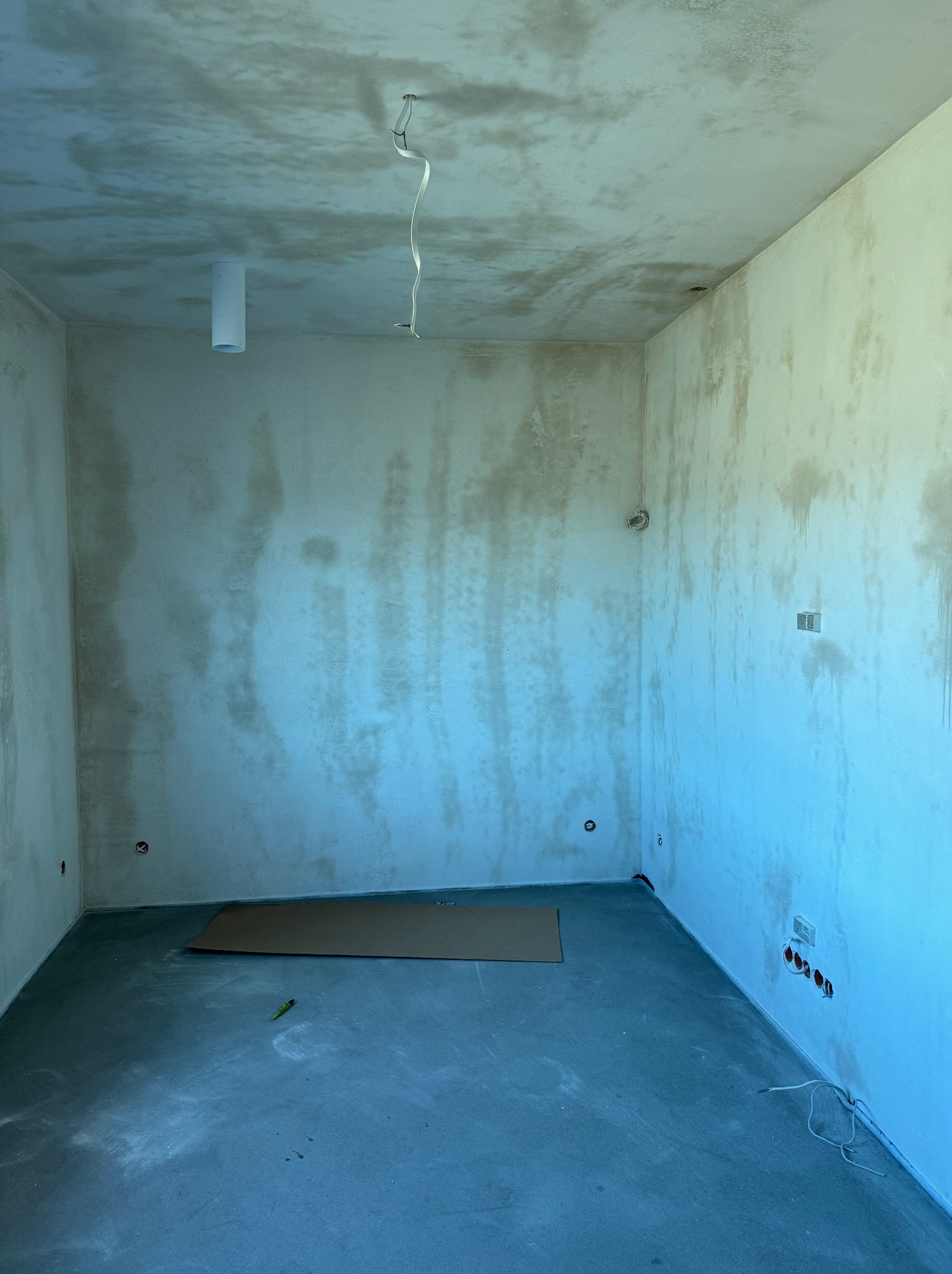 Pokój w trakcie prac wykończeniowych: ściany po szpachlowaniu, surowy beton na podłodze, wystające kable elektryczne, przygotowany do dalszych prac.