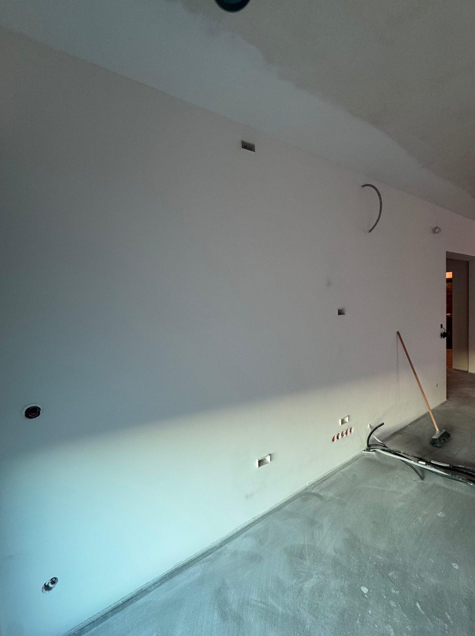 Wnętrze po gładziowaniu ścian i wylewce podłogi, widoczne puszki elektryczne i rury w ścianie, przygotowane do dalszych prac wykończeniowych.