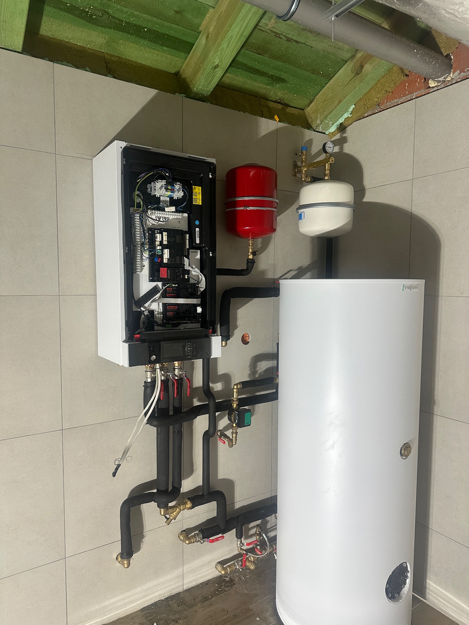 Nowoczesny piec gazowy kondensacyjny z otwartą obudową, widoczne elementy wewnętrzne, podłączony do instalacji z czerwonym i białym zbiornikiem wyrównawczym oraz białym zasobnikiem ciepłej wody,...