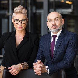 Profesjonalny portret biznesowy: kobieta w czarnej marynarce i mężczyzna w garniturze, oboje z dłońmi splecionymi na oparciu krzesła, na tle nowoczesnego biura.