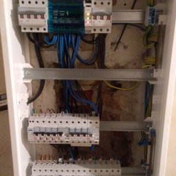 51 Mieczysław Terlecki - Wnętrze białej skrzynki rozdzielczej z bezpiecznikami i przewodami. Widoczne liczne kable w kolorach niebieskim, żółtym i czarnym oraz metalowe szyny montażowe.