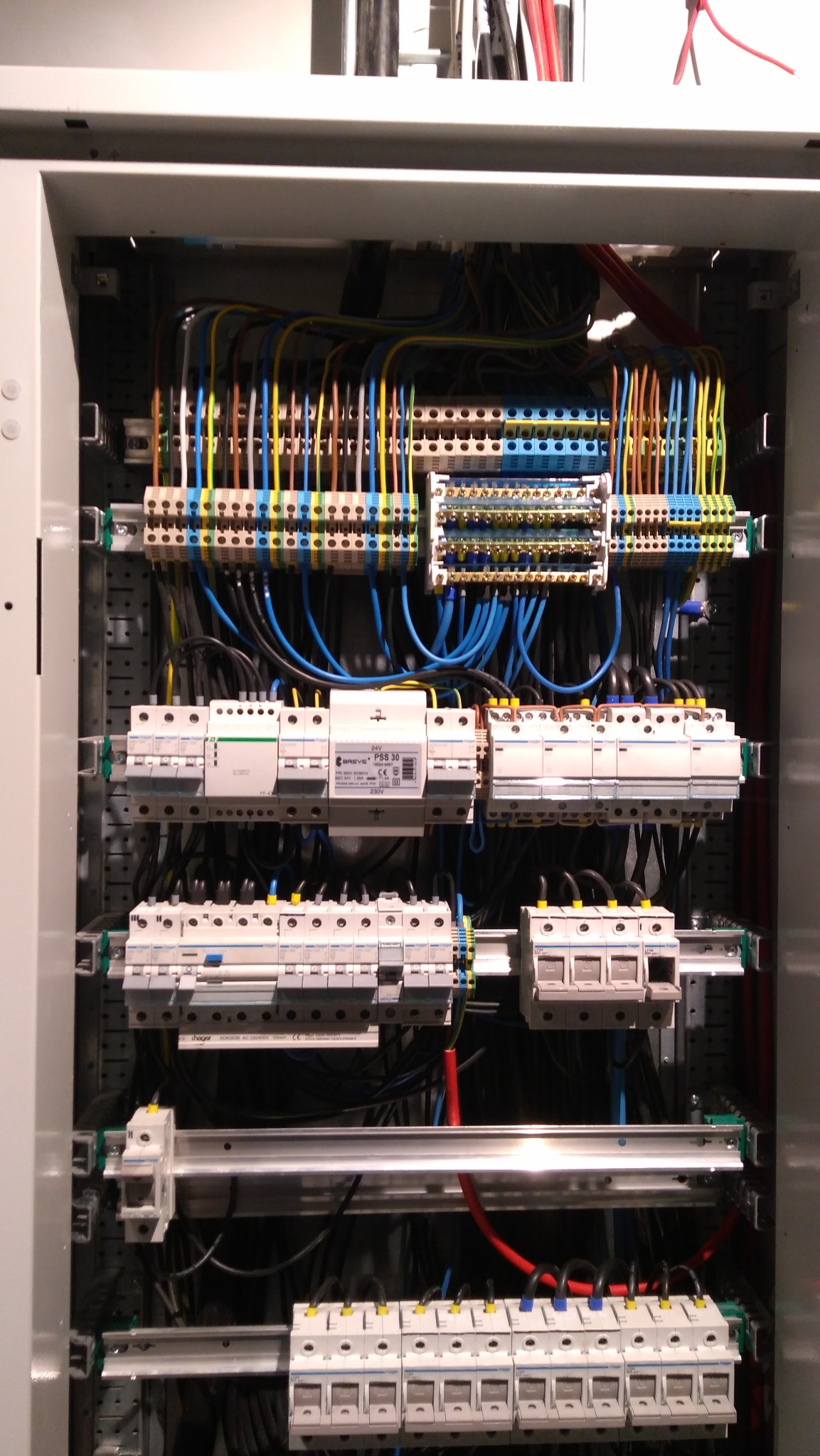 Rozdzielnica elektryczna z zainstalowanymi bezpiecznikami i przewodami w różnych kolorach, widok z bliska, oświetlenie górne.