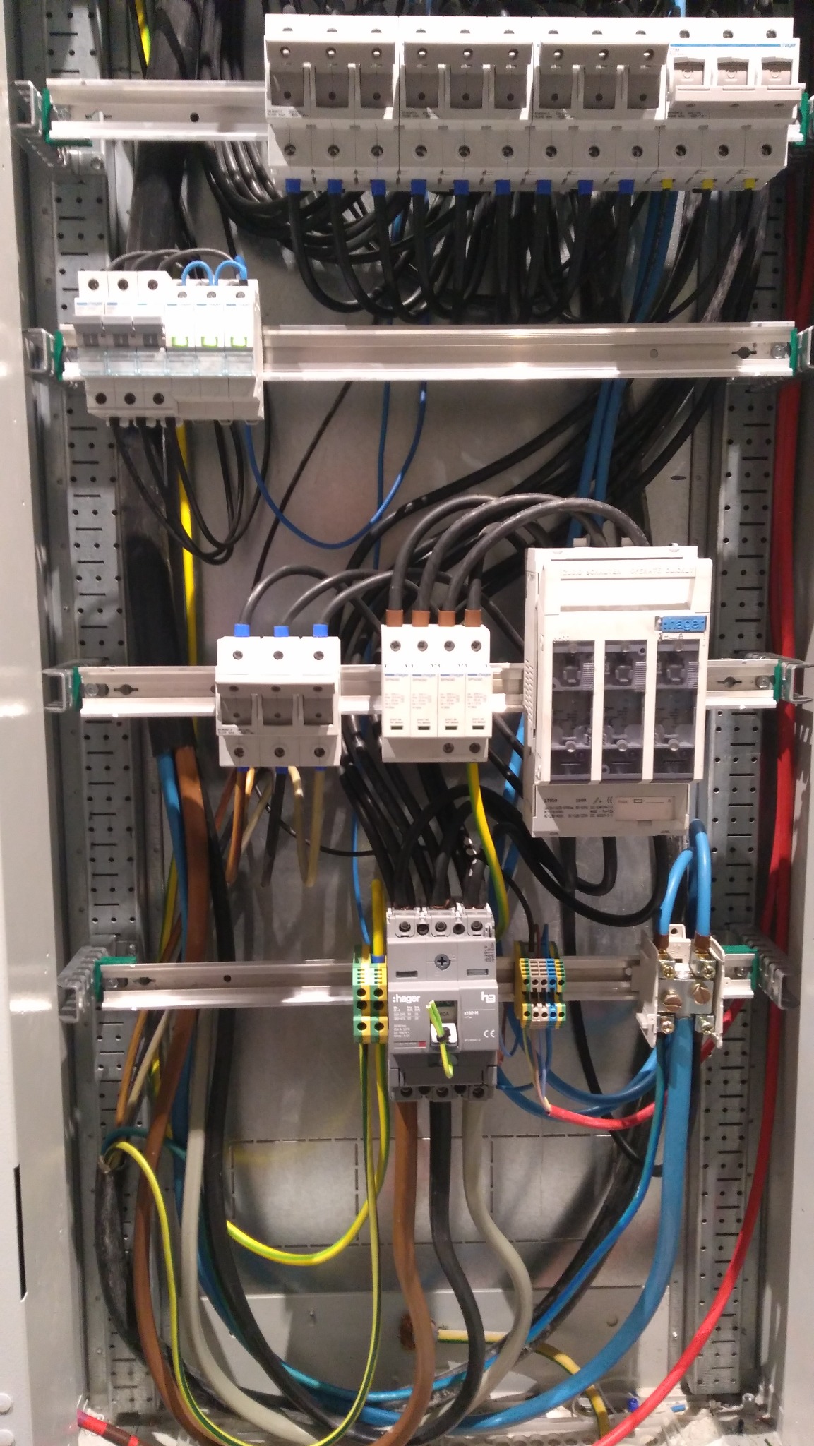 Rozdzielnia elektryczna z widocznymi zabezpieczeniami, przewodami w różnych kolorach i listwami montażowymi, ukazująca zaawansowanie instalacji.