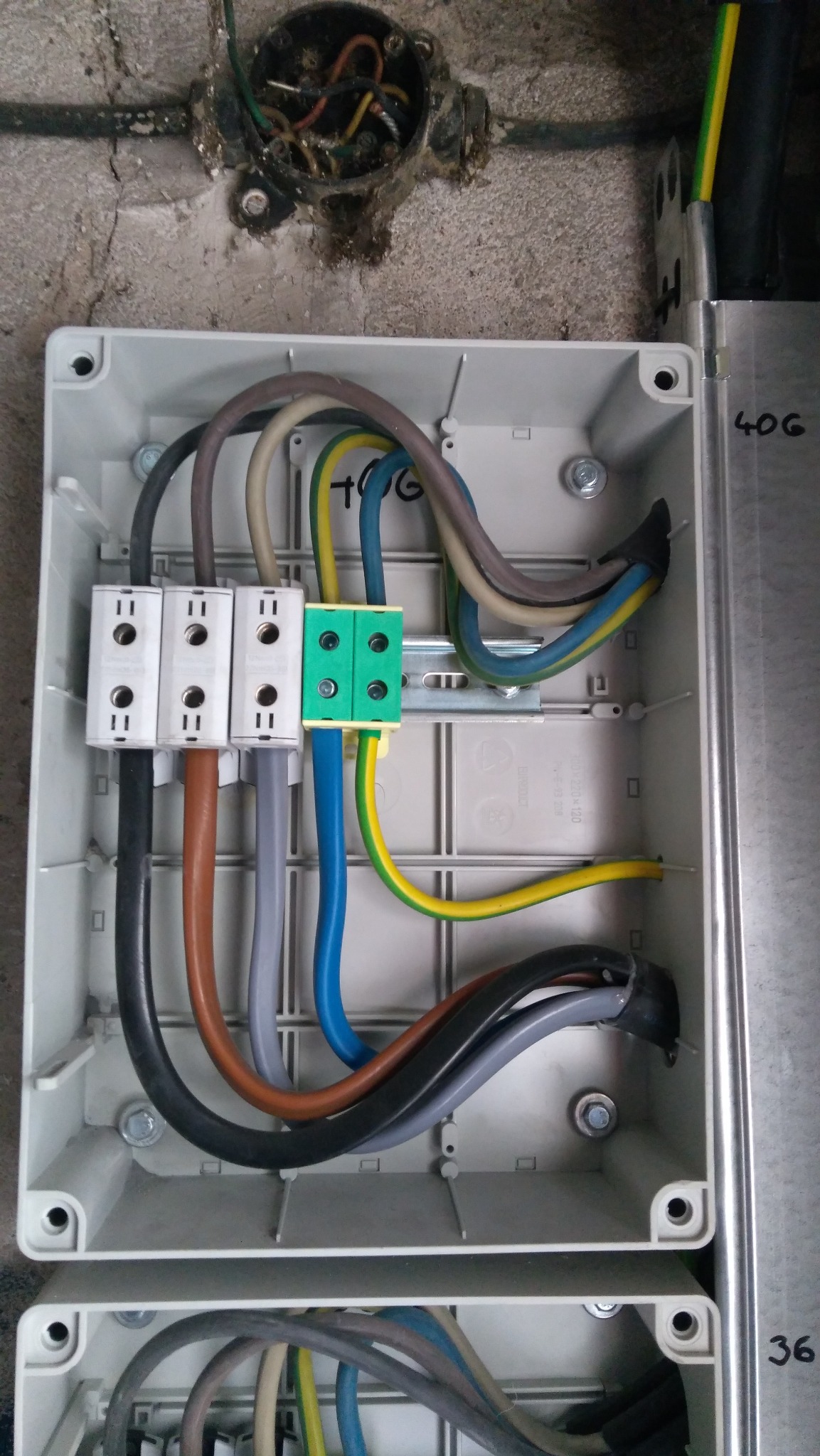 Wnętrze skrzynki elektrycznej z podłączonymi przewodami o różnych kolorach i złączkami, zamontowanej na ścianie. Widoczna stara puszka instalacyjna.