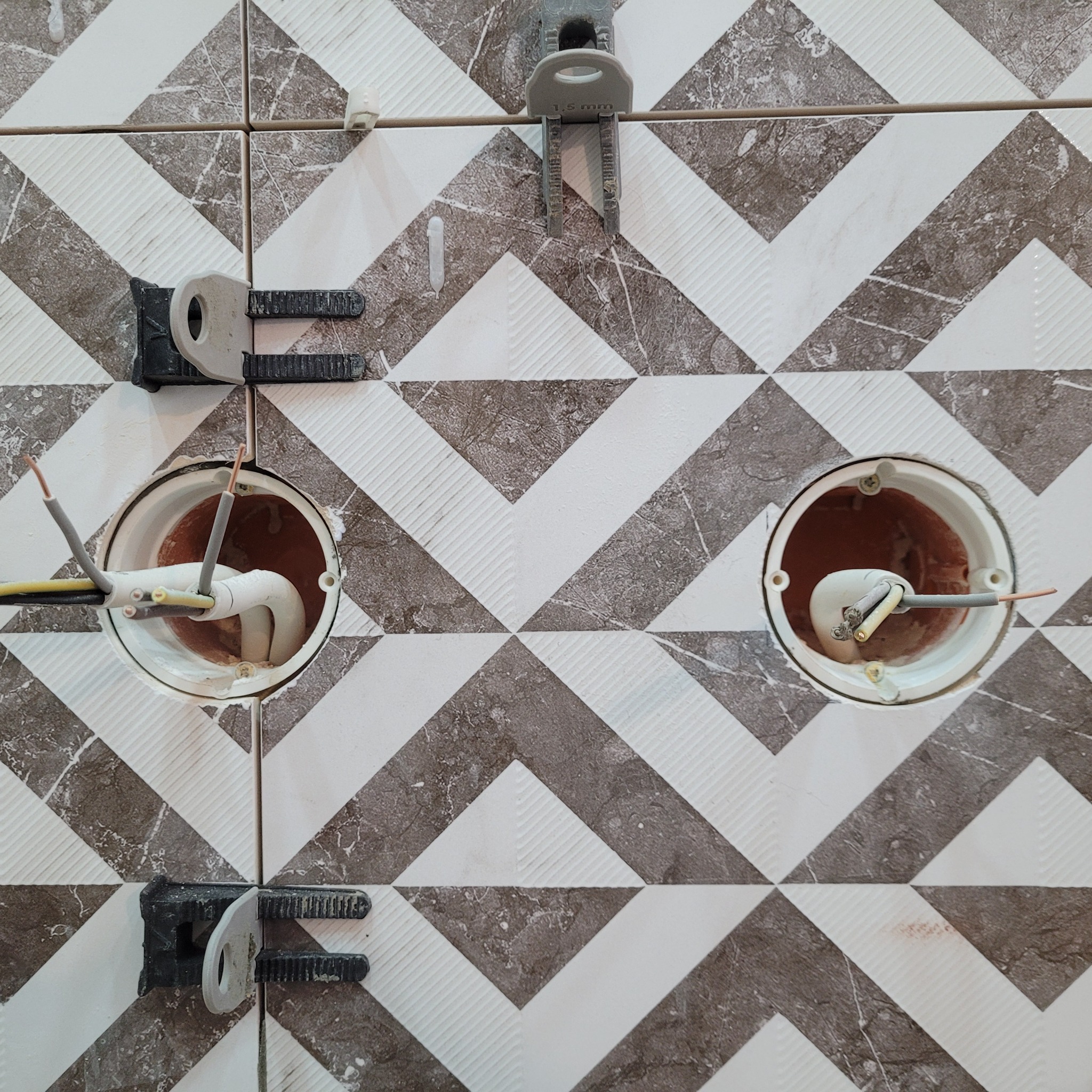 Montaż płytek chevron w łazience, widoczne otwory na puszki elektryczne i system poziomowania płytek.