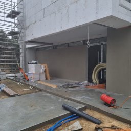 SzwagrBud - Budowa domu w trakcie: ściany z betonu komórkowego, rusztowanie, otynkowana elewacja, przewody wentylacyjne, nagrzewnica gazowa i butla, widoczne materiały izolacyjne.