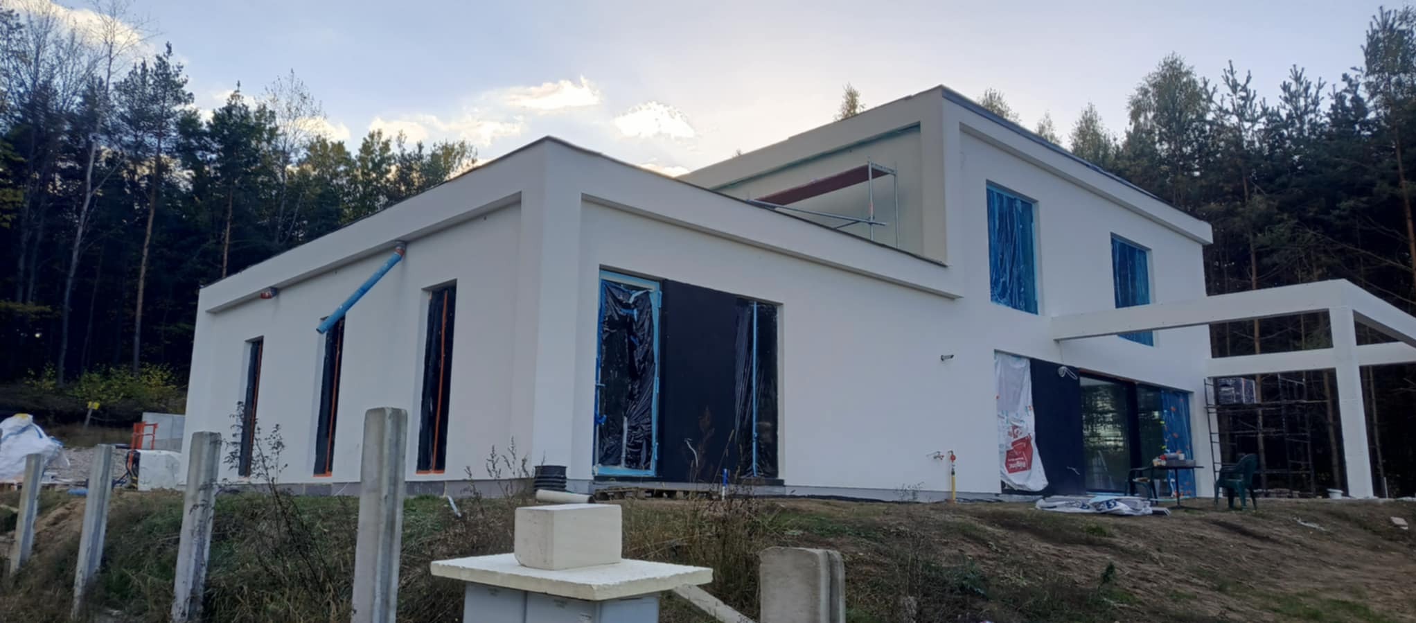 Nowoczesny, biały dom w Białymstoku w trakcie prac elewacyjnych, okna zabezpieczone folią, widoczne rusztowania i materiały budowlane na posesji.