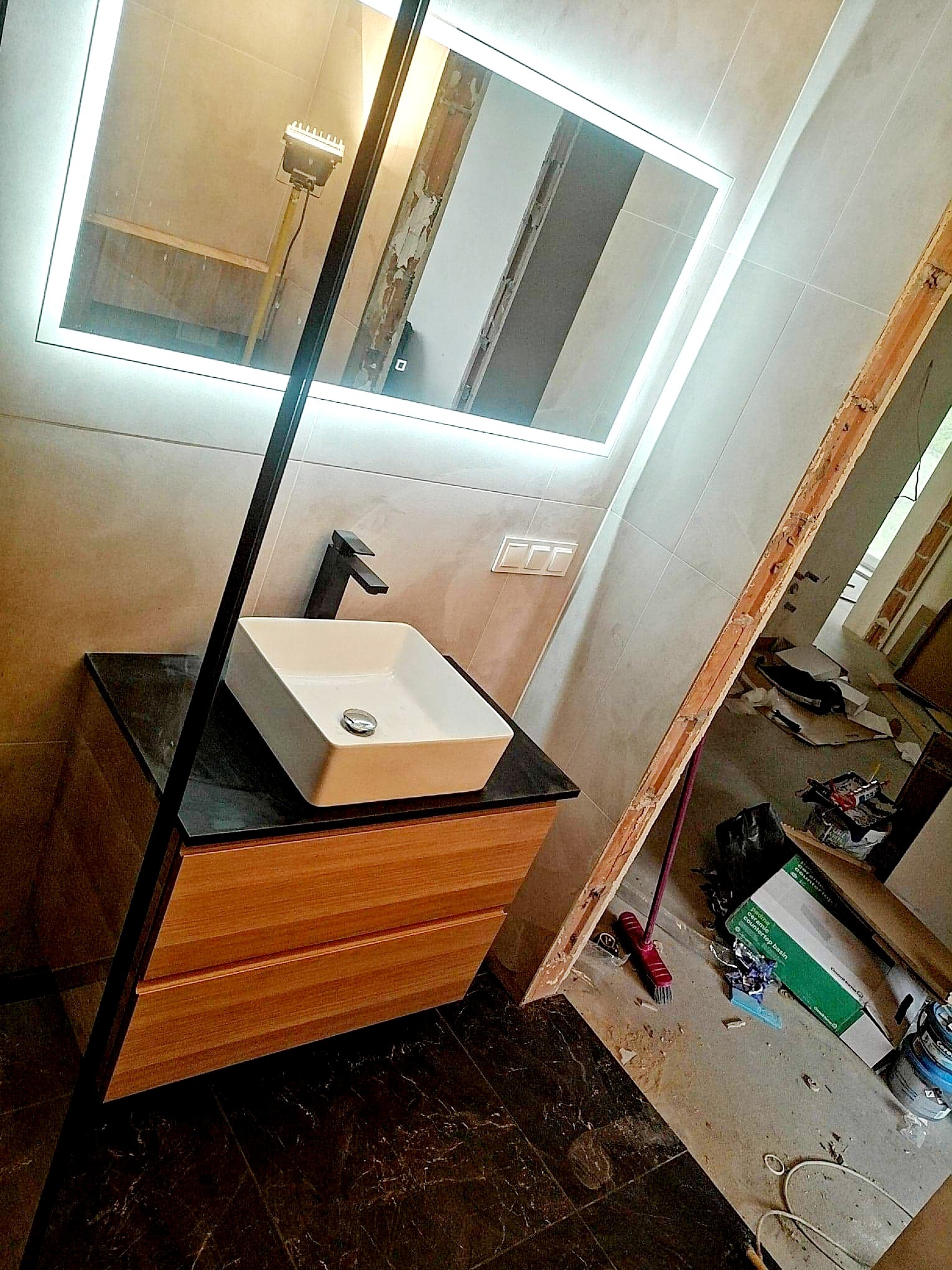 Montaż umywalki nablatowej z czarną armaturą i podświetlanym lustrem w łazience podczas remontu w Busko-Zdroju; widoczne niedokończone ściany i podłoga z ciemnego marmuru.